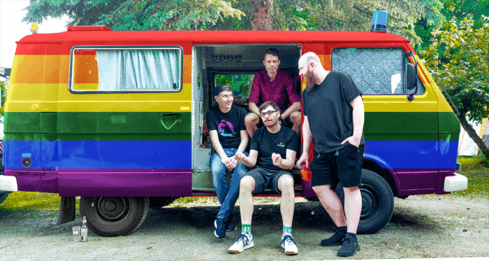 Vier Personen an der geöffneten Seitentür eines in Regenbogenfarben gestrichenen Kleinbusses.